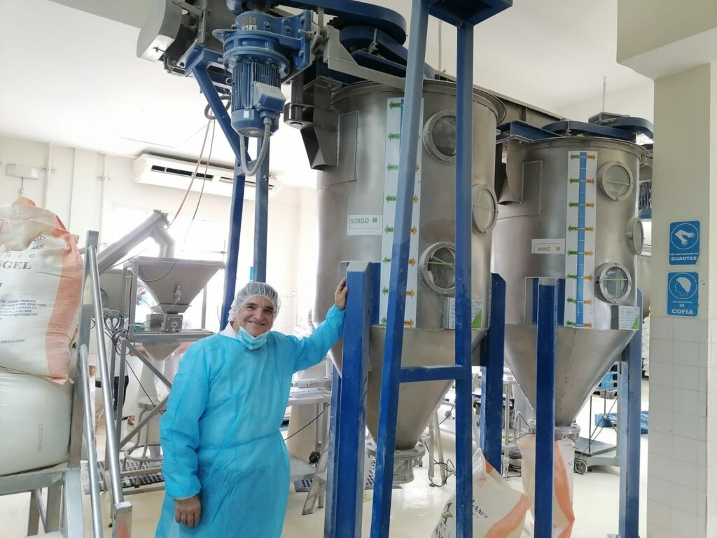 A man in scrubs stands in front of a piece of food processing equipment.