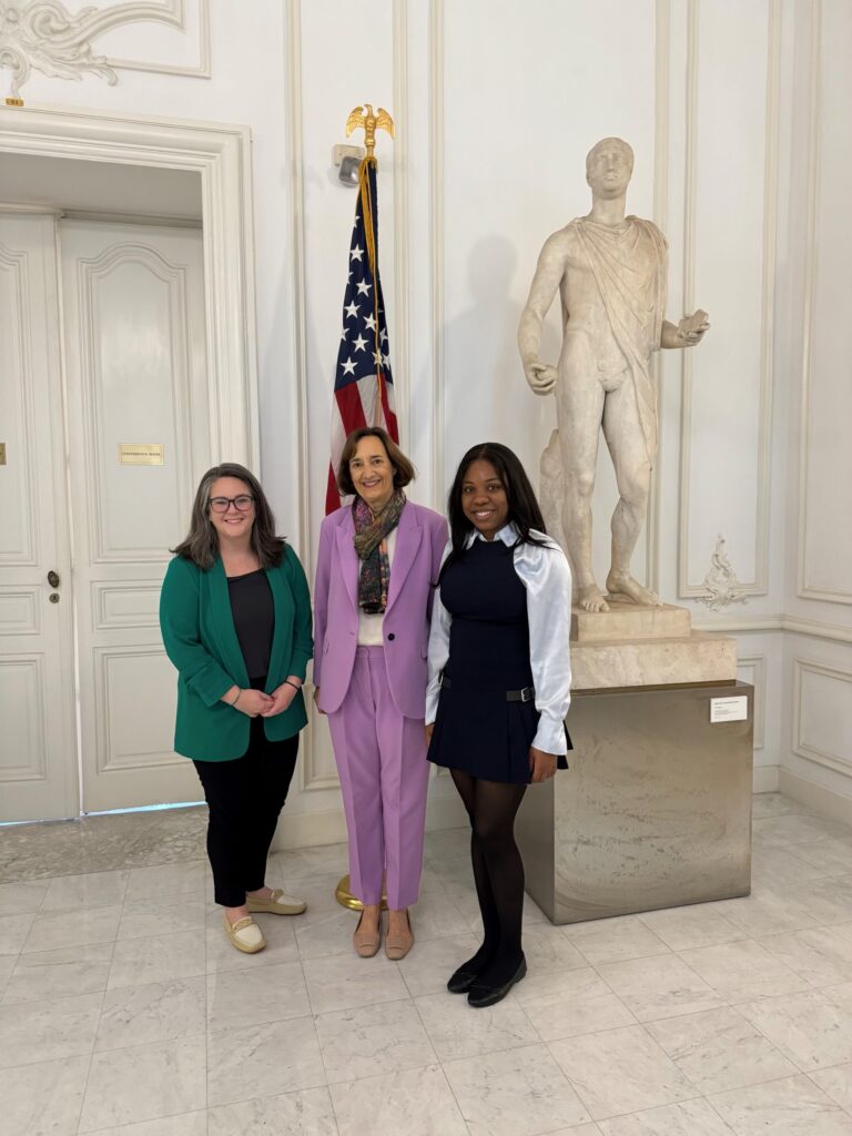 Three people stand in front of a statue and the American flag.