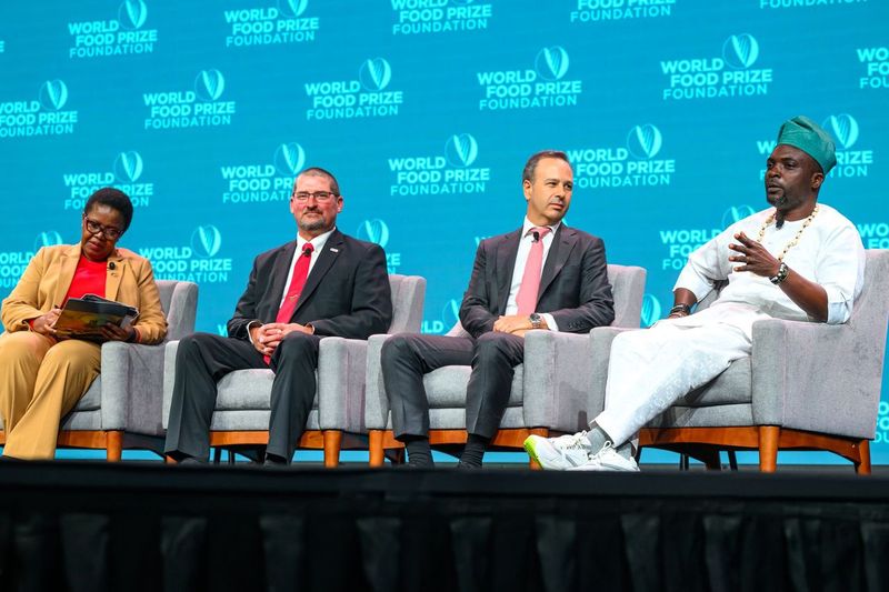 Four panelists sit in chairs in front of a back wall displaying the World Food Prize Foundation logo.