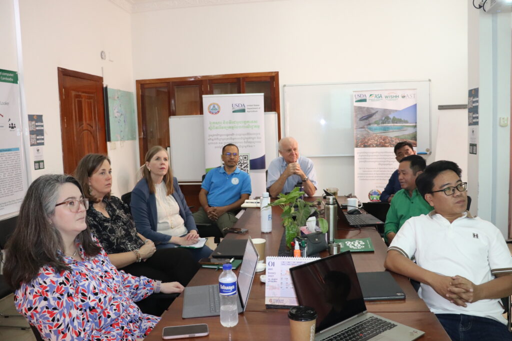 Eight people sit around a table and view a presentation. 